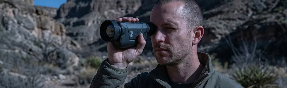 Mand kigger gennem ATN BlazeHunter 635 LRF i klippefyldt terræn